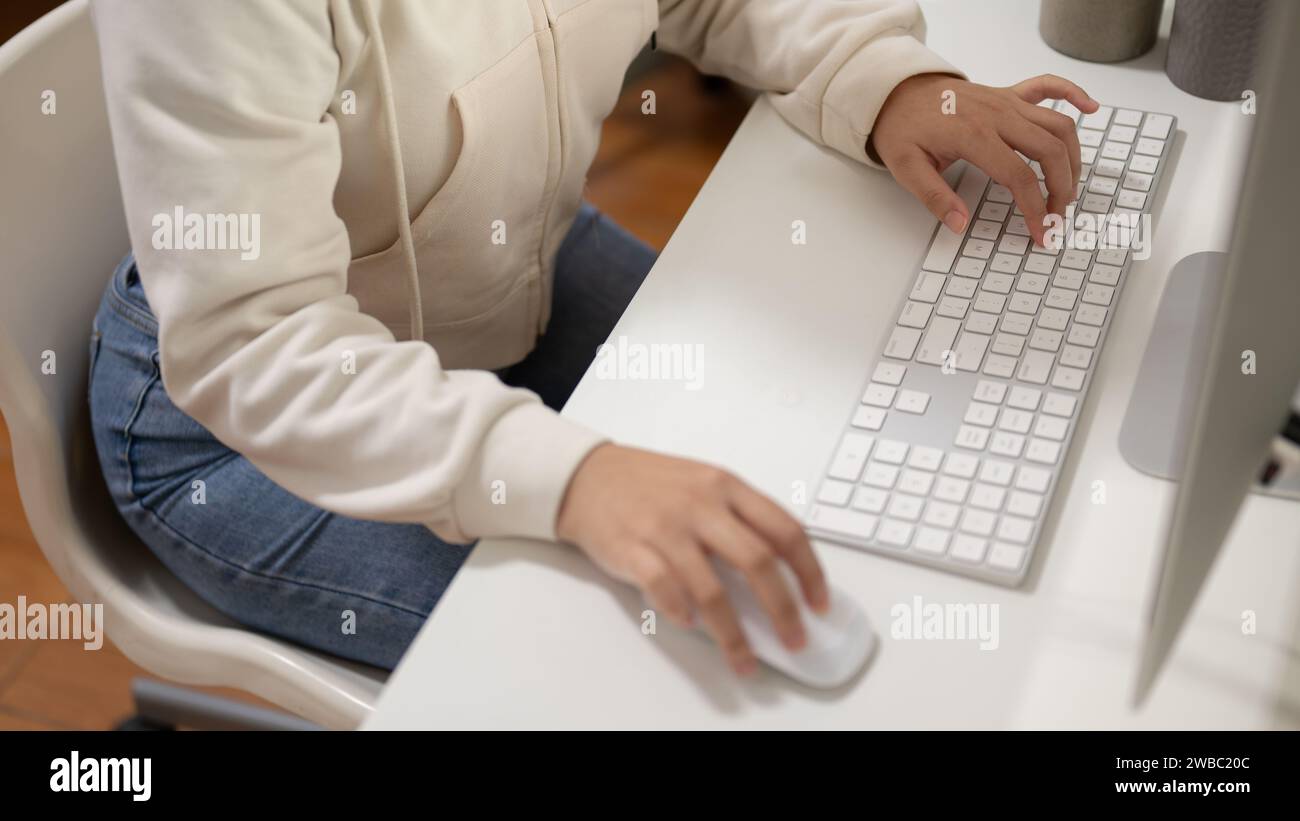 Nahaufnahme einer Büroangestellten oder Studentin in Hoodie arbeitet an ihrem Computer an ihrem Schreibtisch. Menschen- und Technologiekonzepte Stockfoto