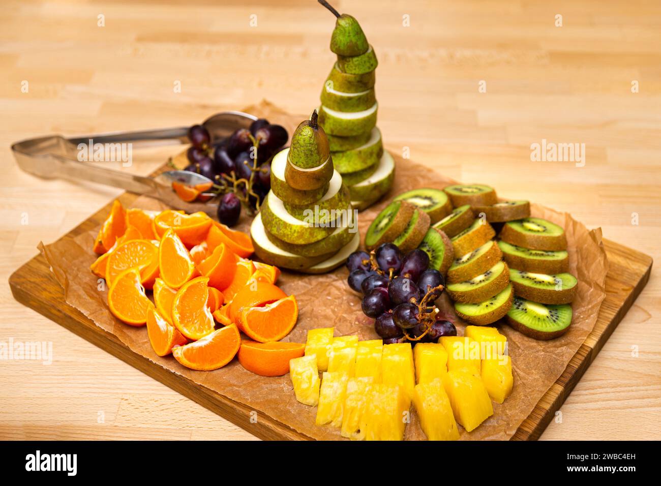 Eine lebhafte Auswahl an frischen Früchten mit einem Herzstück einer spiralgeschnittenen Birne, umgeben von Orangen, Kiwis, Trauben und Ananas auf einem Holz Stockfoto