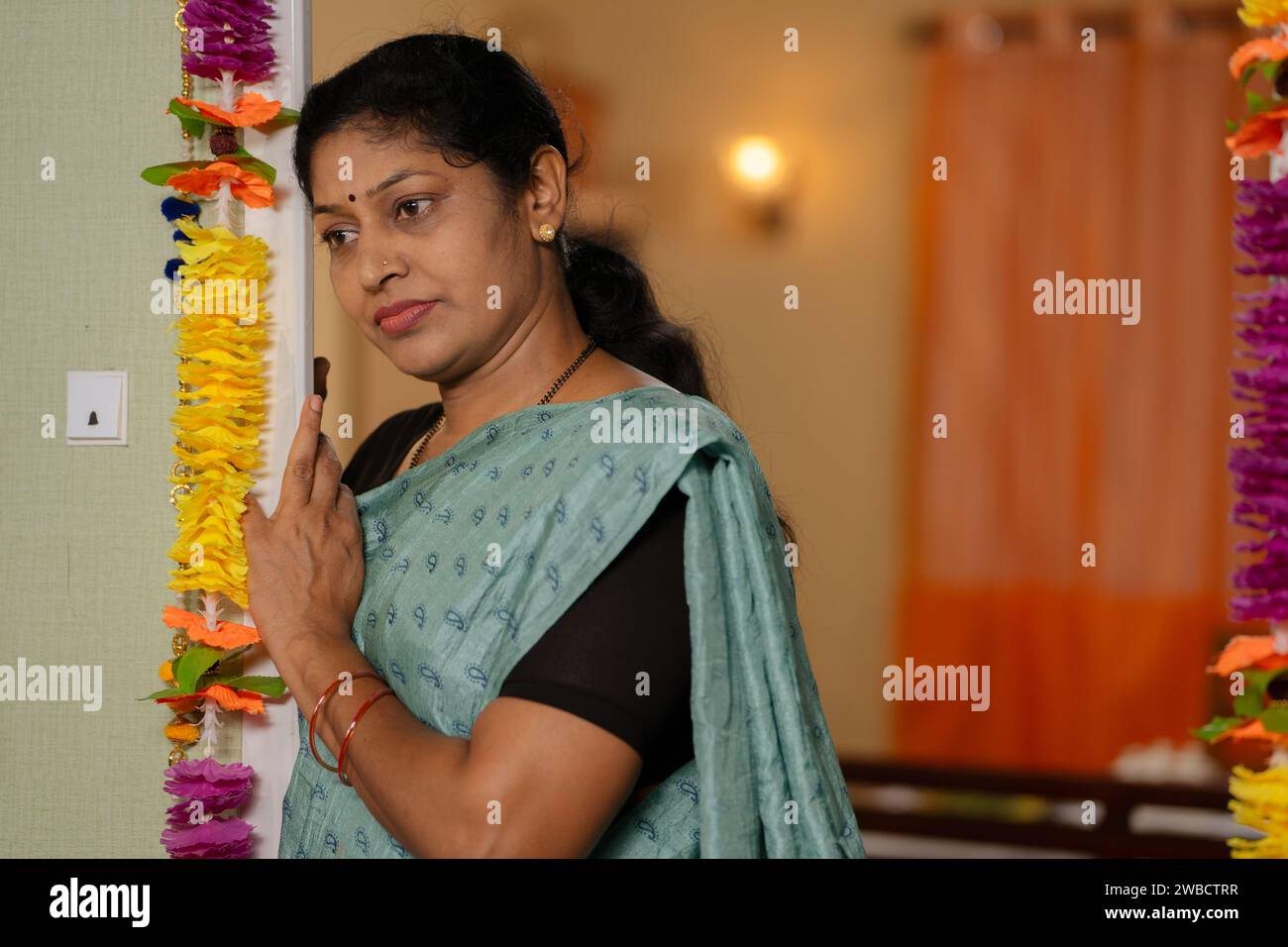 Eine nachdenkliche indische Frau, die in der Nähe der Tür wartete und sich nach einem Mann oder nach Kindern umsah - Vorstellung von einer vermissten Familie, einer Hausfrau und besorgt Stockfoto