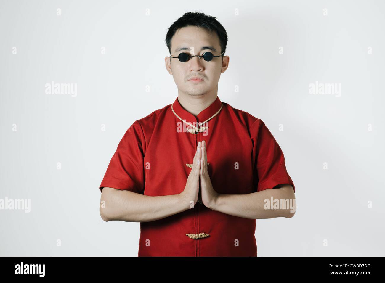 Asiatischer Mann, der traditionelle Tracht trägt, gibt der Kamera auf weißem Hintergrund eine Namaste oder Begrüßungs- oder Begrüßungsgeste. Frohes Chinesisches Neujahr. Stockfoto