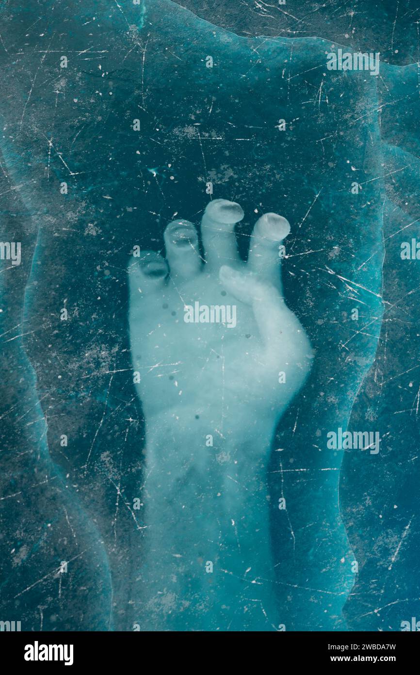 Eine Nahaufnahme zeigt die Umrisse eines menschlichen Fußes unter einer strukturierten, durchscheinenden blauen Eisschicht, die eine Mischung aus Gelassenheit und Einengung hervorruft. Stockfoto