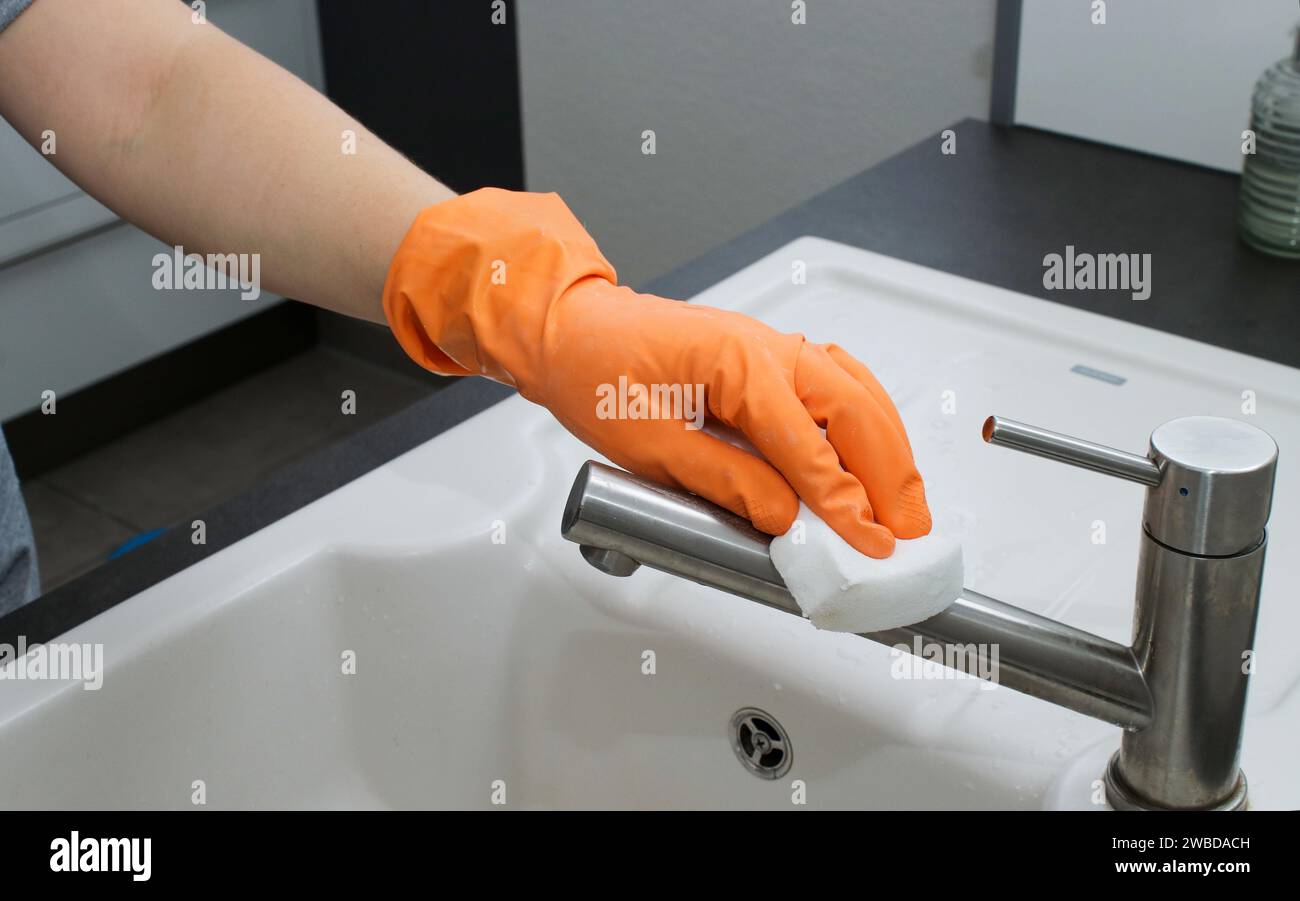 Nahaufnahme der Hand der Frau im orangefarbenen Handschuh, der Küchenspüle reinigt Stockfoto