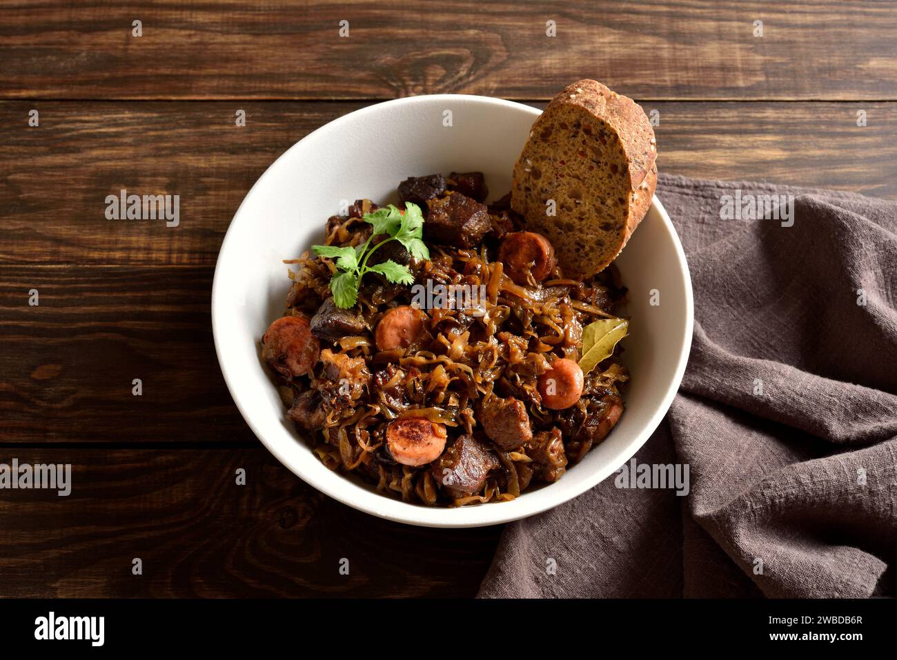 Gedünsteter Kohl (polnische Bigos) mit Sauerkraut, Pilzen, Räucherfleisch und Gewürzen in einer weißen Schüssel auf rustikalem Holztisch. Nahansicht Stockfoto