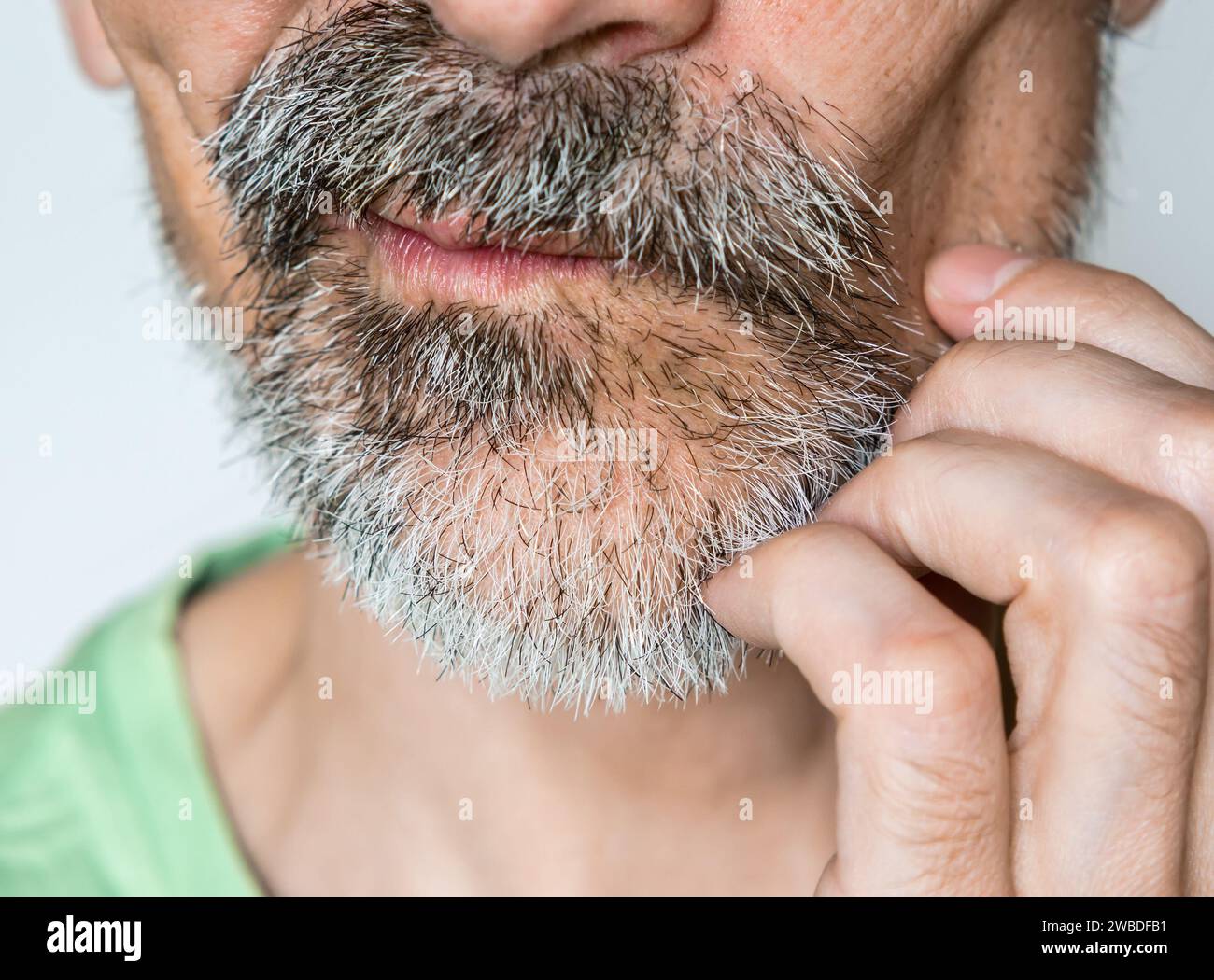 Ein Mann mittleren Alters kratzt nachdenklich sein unrasiertes Gesicht aus der Nähe Stockfoto