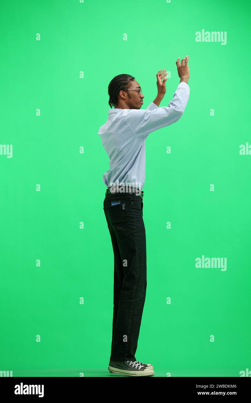 Ein Mann in einem grauen Hemd, auf grünem Hintergrund, in voller Höhe, mit den Armen winkend Stockfoto