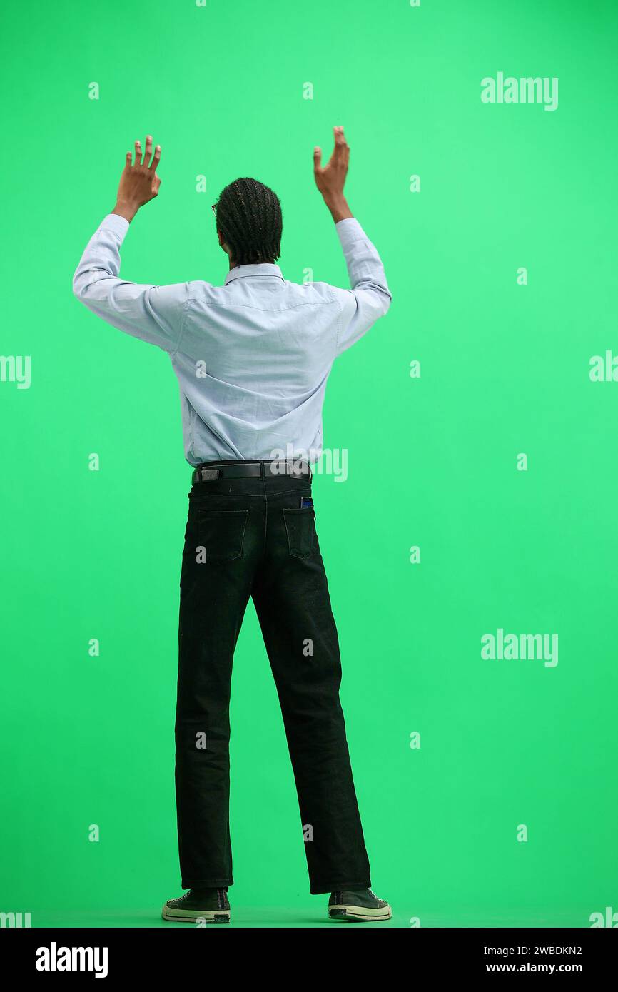 Ein Mann in einem grauen Hemd, auf grünem Hintergrund, in voller Höhe, mit den Armen winkend Stockfoto