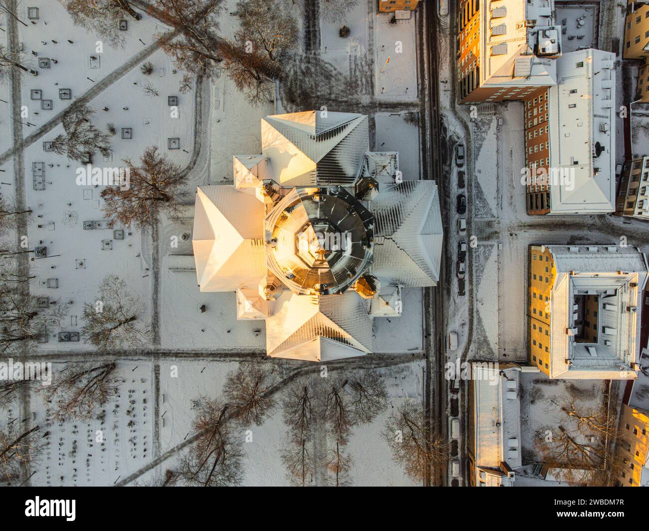 Vertikale Luftaufnahme des Daches einer Kirche in Stockholm, Schweden, mit Schnee und Sonnenlicht am ersten Morgen. Gelbe und orangene Farben. Fußwege. Stockfoto