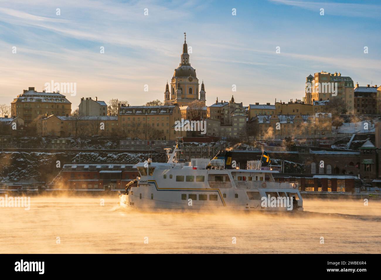 Ein Pendlerboot, das an einem sehr kalten Morgen an der Kirche Katarina in Stockholm vorbeifährt, wo das Meer raucht und Schnee und Frost sichtbar sind Stockfoto