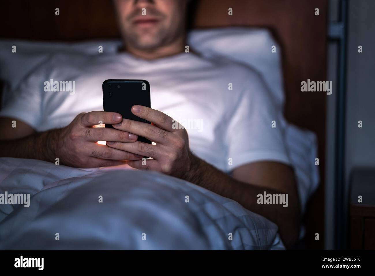 Telefon nachts im Bett. Mann mit Smartphone, bevor er schläft. Geheime SMS schreiben, betrügen oder lange arbeiten. Glücklicher Kerl, der Online-Nachrichten durchsucht. Stockfoto