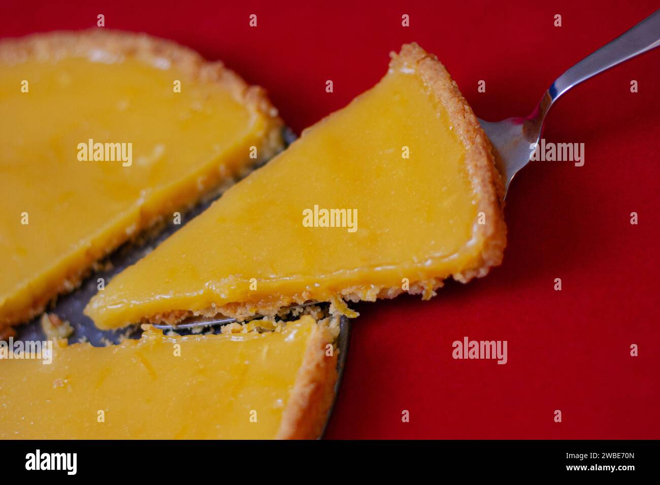 Spatel mit einer Scheibe köstlicher Zitronentorte auf rotem Hintergrund, Blick von oben Stockfoto