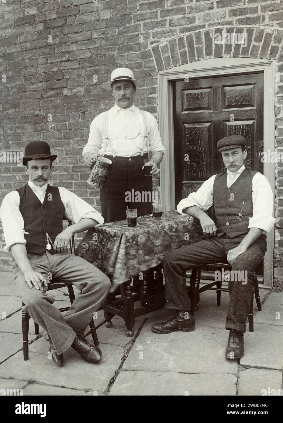 Drei britische Trinker oder Männer, die in der Straße vor der Terrasse des Brick House trinken England Großbritannien. Vintage- oder historische Schwarzweiß- oder Schwarzweiß-Fotografie c1900 Stockfoto