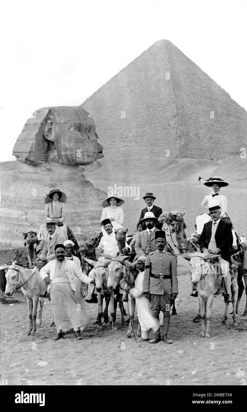 Edwardianische Touristen posieren mit Kamelen und ihren Fahrern vor der Großen Pyramide und der Sphinx in Gaza, Ägypten. C1910 Vintage- oder historische Schwarzweiß- oder Schwarzweiß-Fotografie Stockfoto