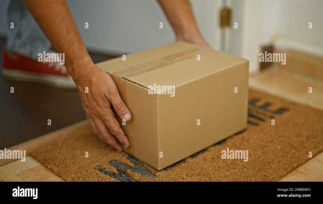 Die Hand eines Mannes legt einen Karton auf eine Fußmatte in einem Haus, symbolisiert Lieferung oder Bewegung. Stockfoto