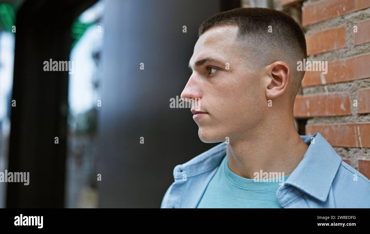 Ein Profilporträt eines jungen hispanischen Mannes draußen mit einem Hintergrund der Stadtstraße, das Selbstvertrauen und Attraktivität zeigt. Stockfoto