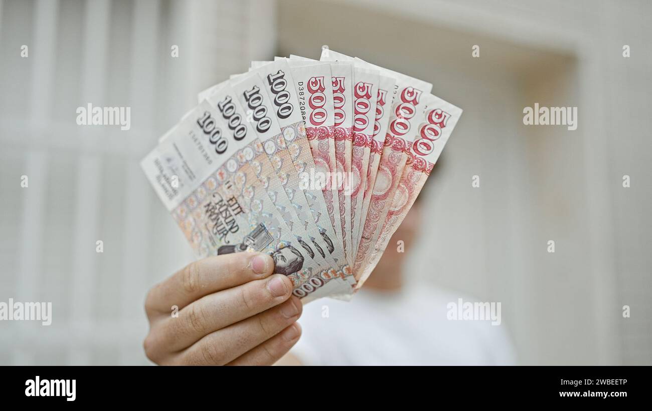 Hübscher junger hispanischer Teenager, der fröhlich isländische Kronen im Freien auf der städtischen Straße hält und seine erste Investition in authentische nordi tätigt Stockfoto