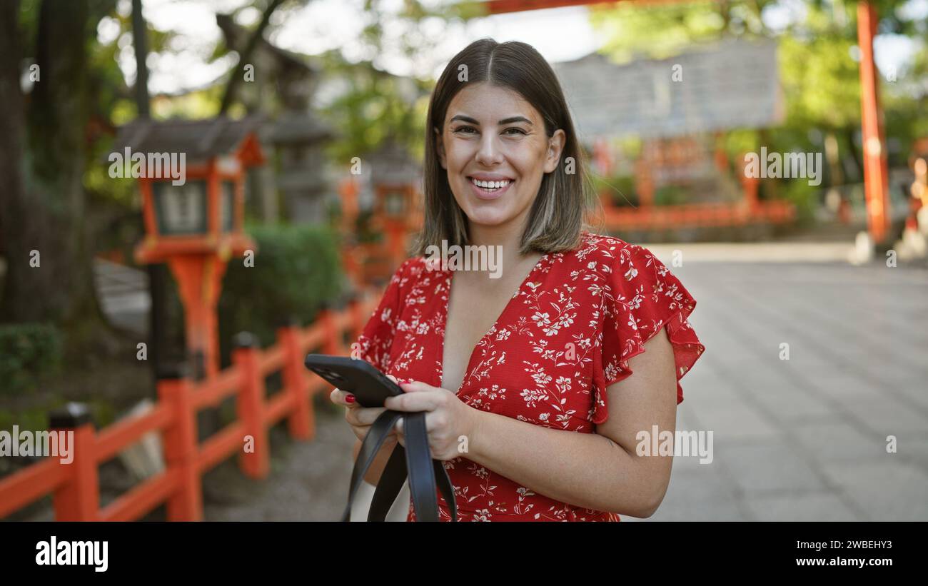 Fröhlich schöne hispanische Frau genießt ihr Telefon, lächelt und schreibt im yasaka Tempel, kyoto Stockfoto