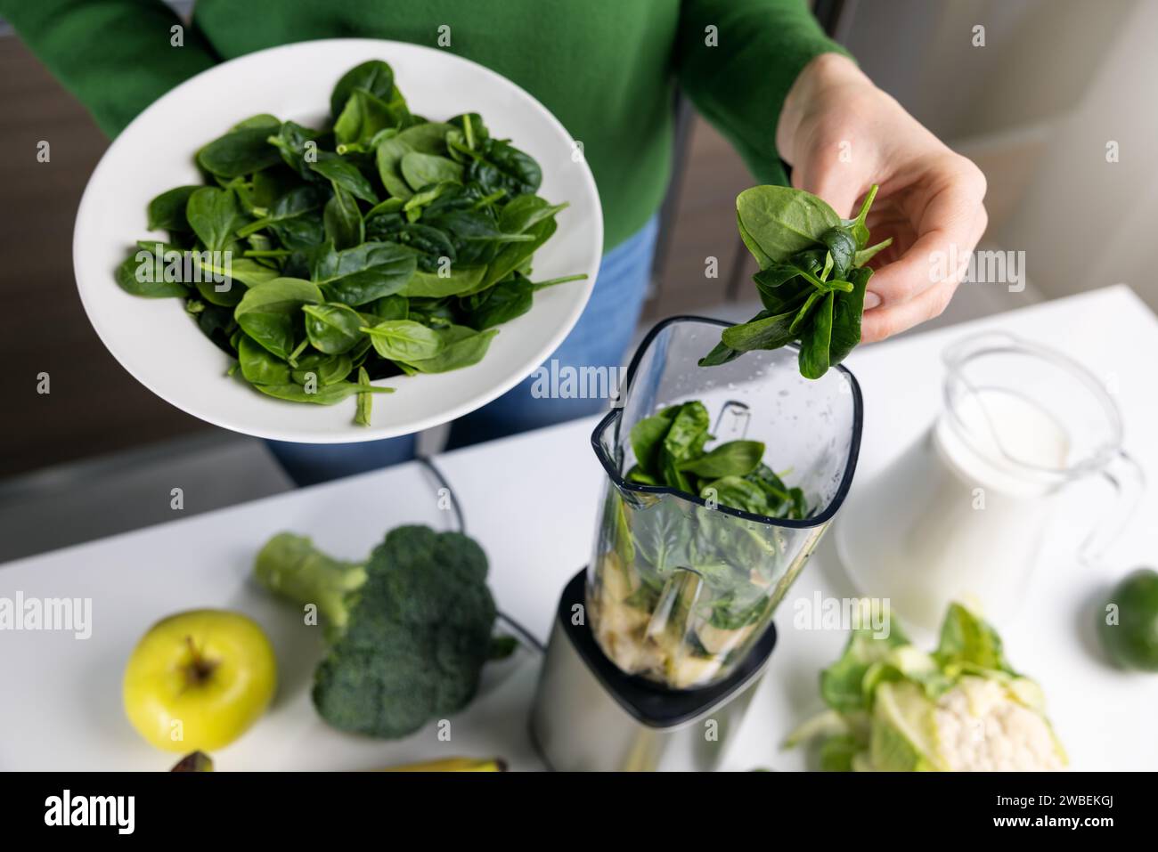 Frau gibt frischen grünen Spinat in den Mixer, um gesunden Detox Smoothie aus Gemüse und Obst in der Küche zu machen Stockfoto