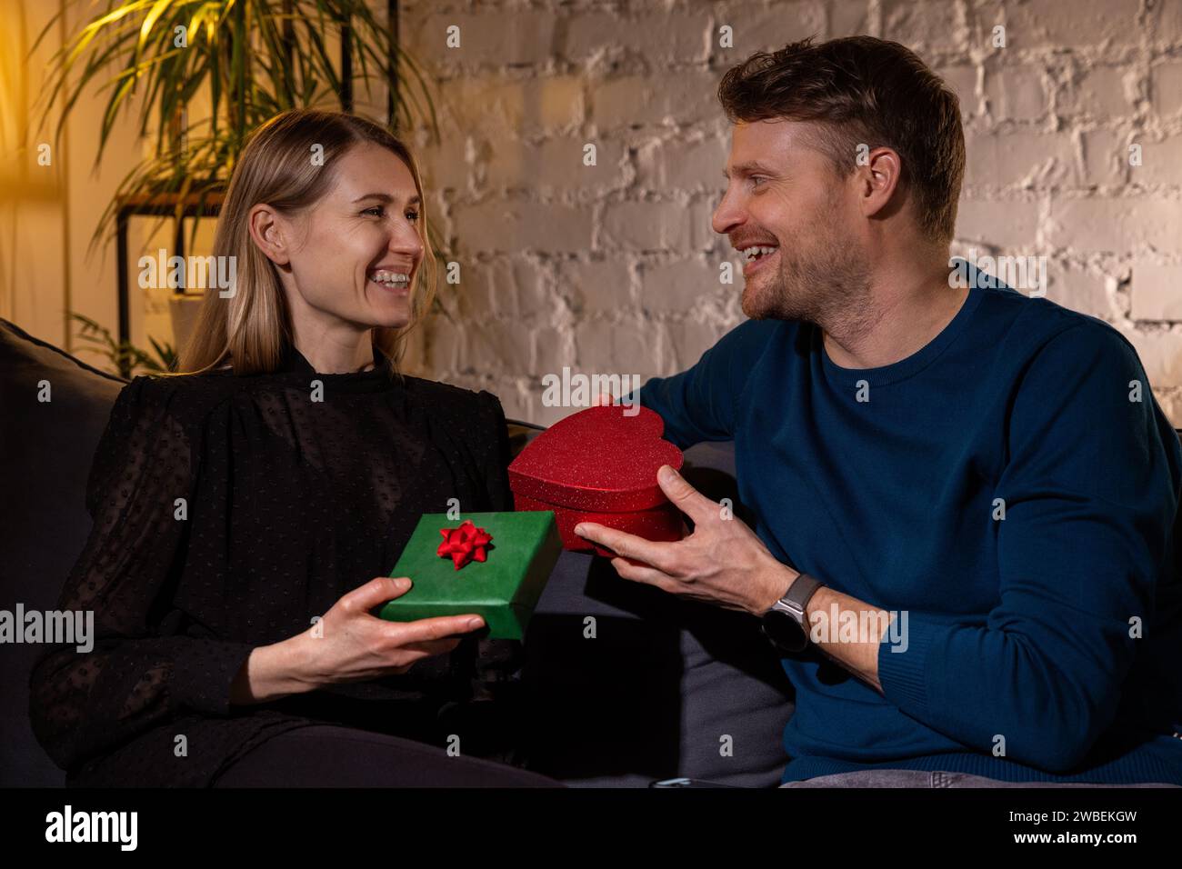 Ein romantisches Paar tauscht sich mit Überraschungsgeschenken aus, während es zu Hause auf dem Sofa sitzt. Geschenk zum valentinstag oder Hochzeitstag Stockfoto