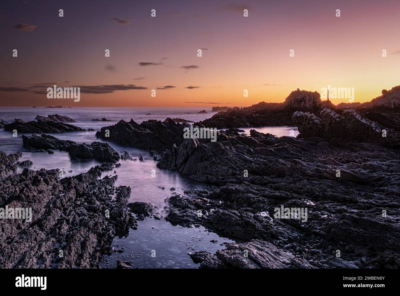 Goldener Sonnenaufgang in der Bucht von Kaikoura. Niedriger Blick auf die Strandfelsen, die Pools, den klaren, goldenen Himmel und ein paar Wolken Stockfoto