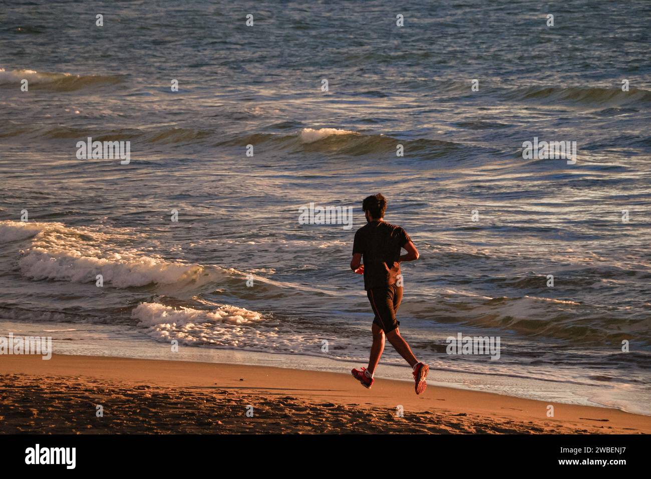 Ein Mann, der am Strand läuft, Mann im Meer läuft, Meer im Hintergrund Stockfoto