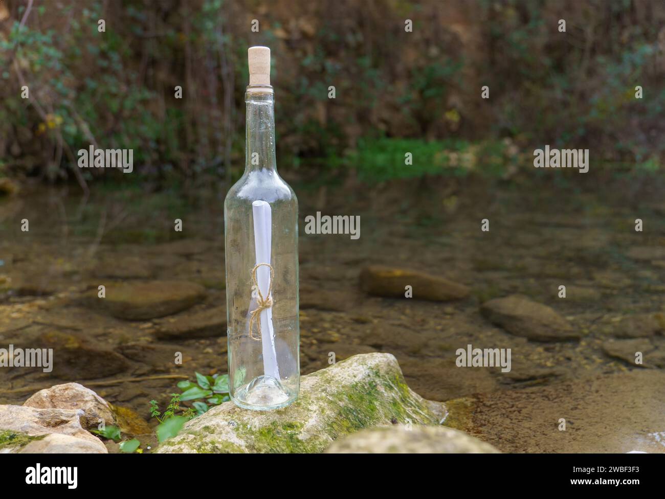 Glasflasche mit einer Botschaft auf einem Felsen am Ufer eines Sees Stockfoto