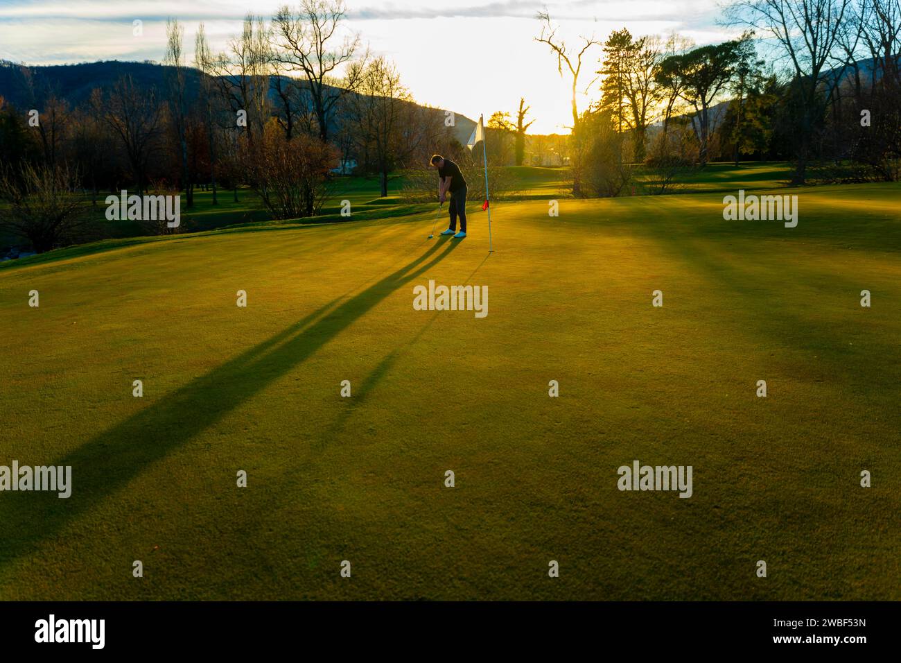 Männliche Golferkonzentration auf dem Putting Green On Golfplatz bei Sonnenuntergang mit Schatten in der Schweiz Stockfoto