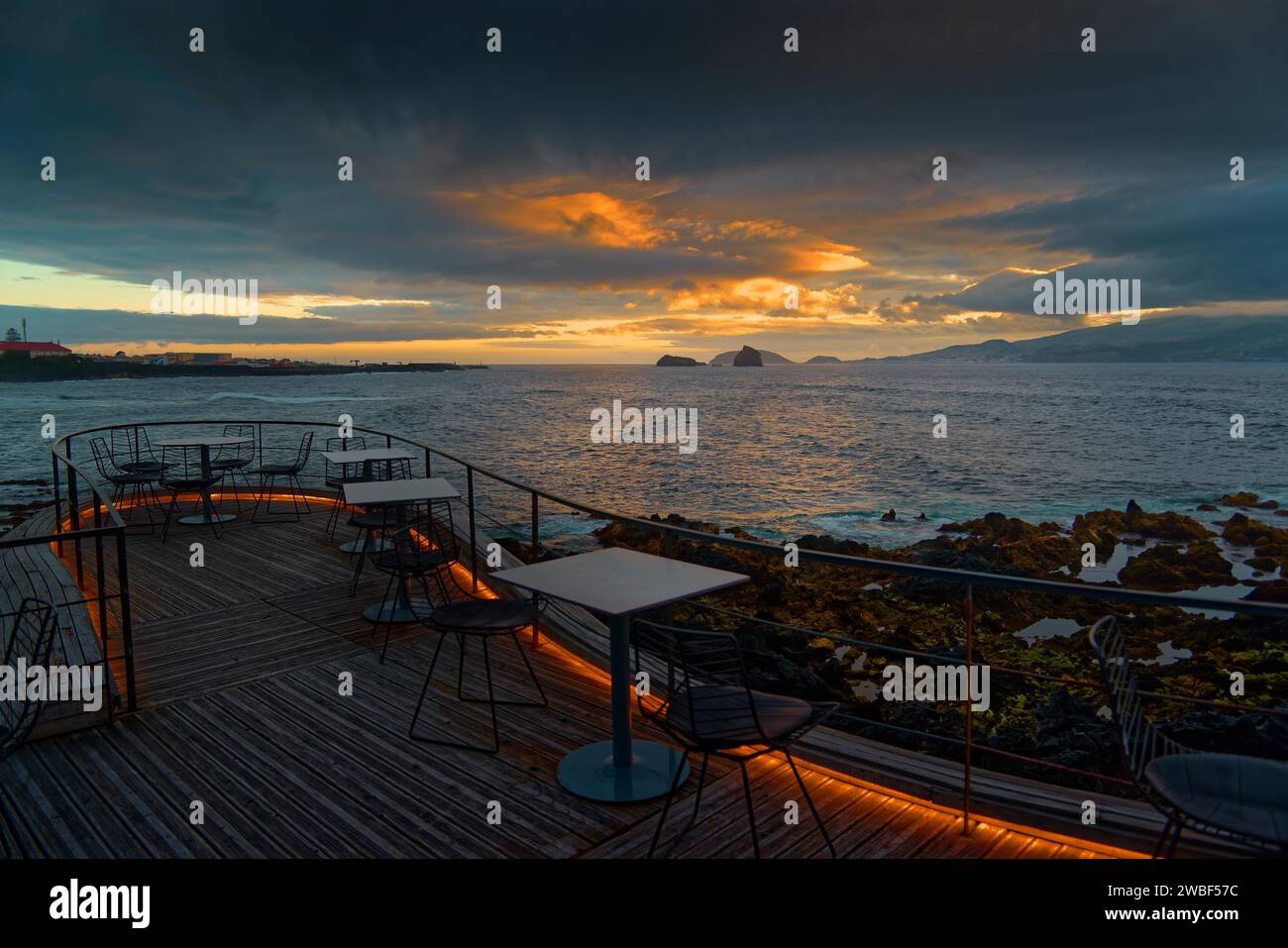 Terrasse der Cella Bar mit Blick auf die Küste von Madalena und die ferne Insel Faial bei Sonnenuntergang unter dramatischen Wolken, Madalena, Pico, Azoren Stockfoto