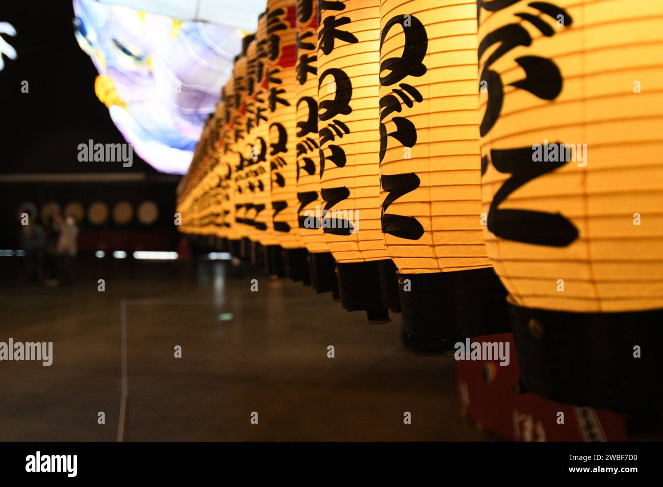 Eine Linie gelber Papierlaternen mit asiatischem Schriftzug hing in einem traditionellen Innenraum des Gebäudes Stockfoto