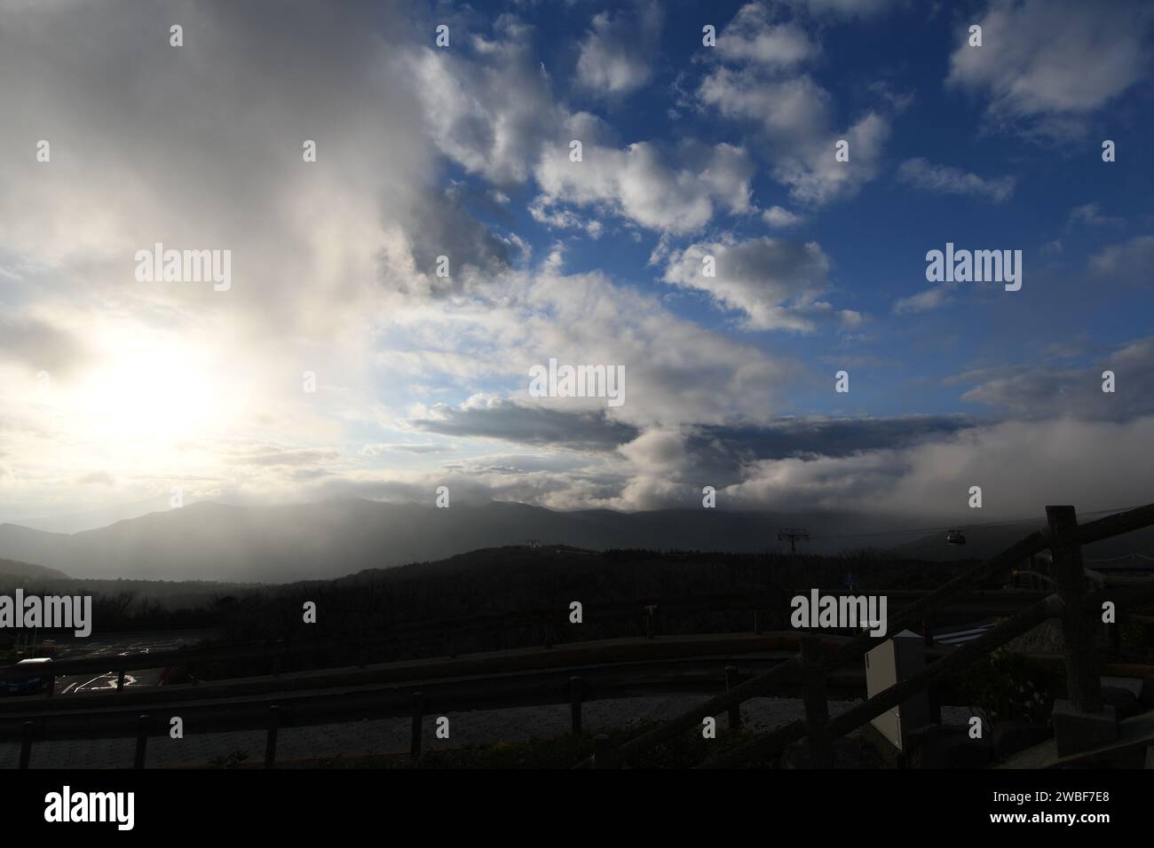 Eine sonnenumwobene Silhouette erleuchtet einen ruhigen blauen Himmel mit schimmernden Wolken, die einen auffälligen Kontrast vor dem Hintergrund des Horizonts bilden Stockfoto