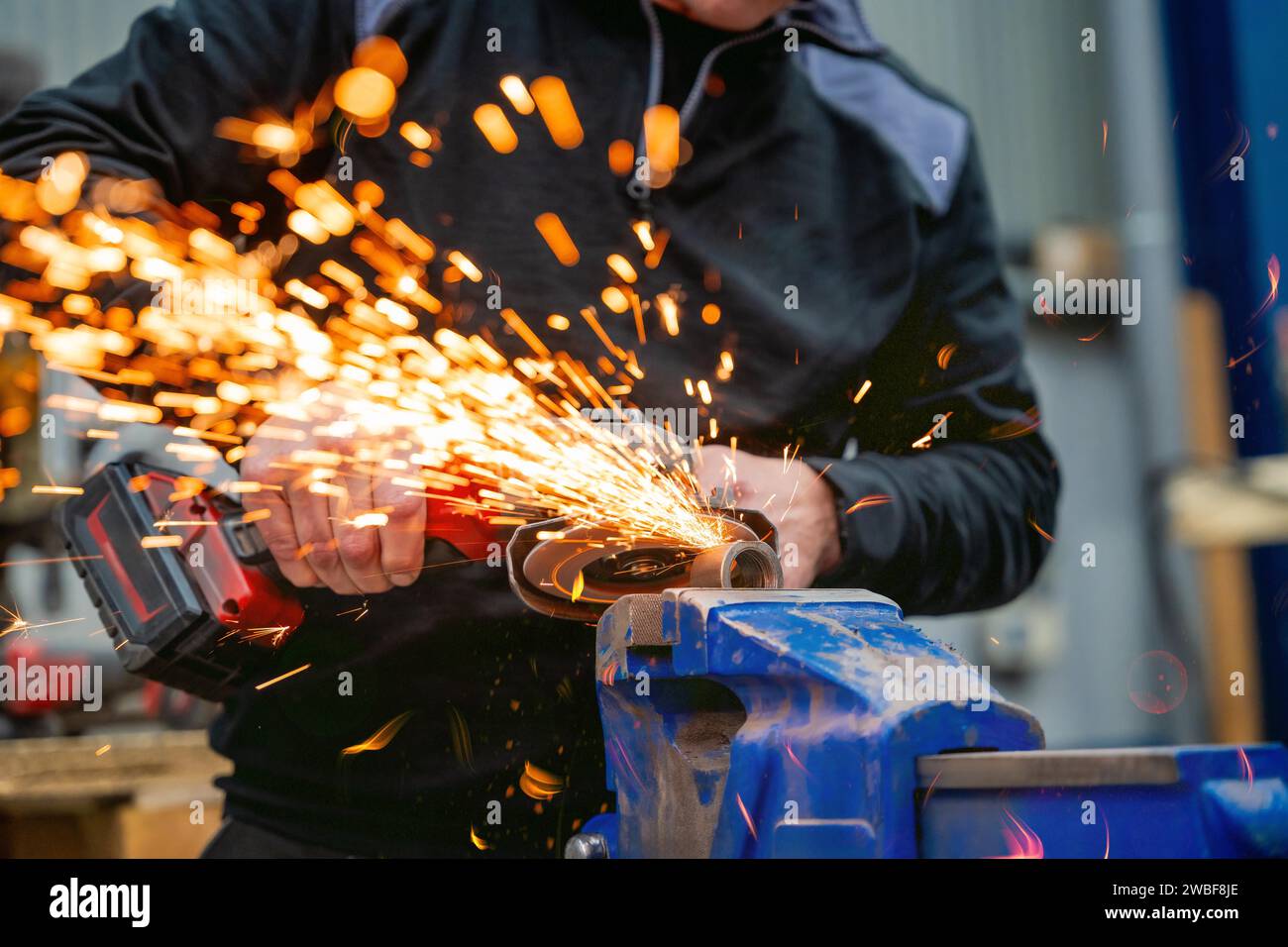 Funken fliegen, während ein Arbeiter im Werk mit einem elektrischen Schleifwerkzeug an einer Stahlkonstruktion arbeitet Stockfoto