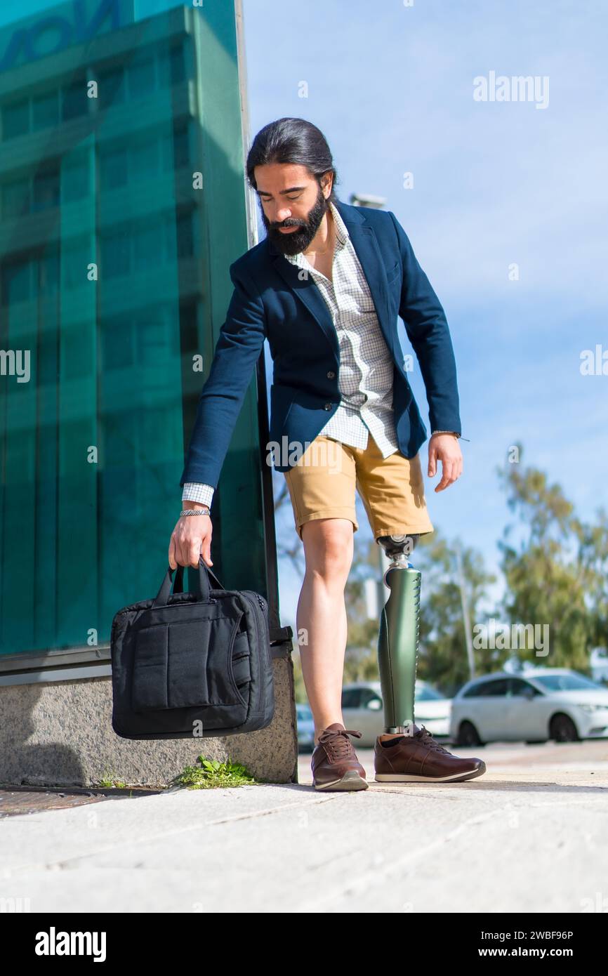 Vertikales Foto eines Geschäftsmannes mit Beinprothese, der draußen eine Laptoptasche auf dem Boden lässt Stockfoto
