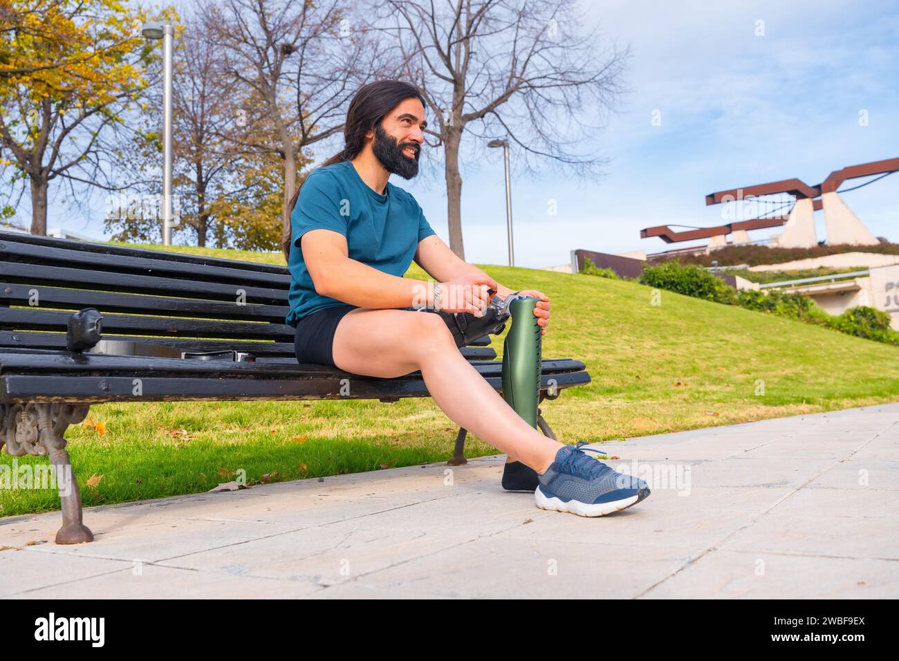 Adaptiver männlicher Sportler, der sein künstliches Laufbein auf einer Parkbank justiert Stockfoto