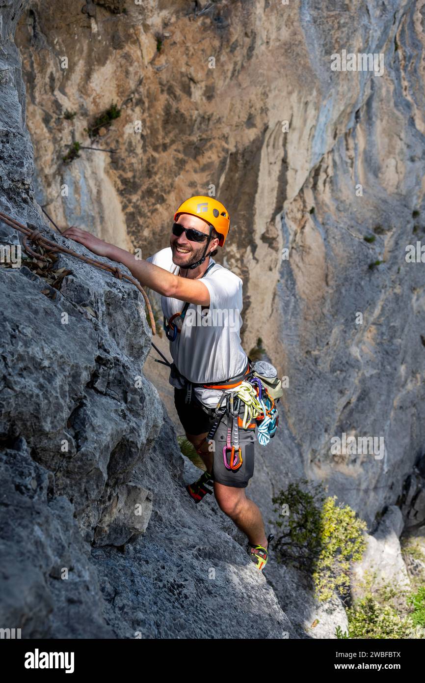 Ein Kletterer mit Helm und Sicherheitsausrüstung klettert an einer steilen Felswände, alpines Klettern mit Seil, Arco, Italien, KI generiert Stockfoto