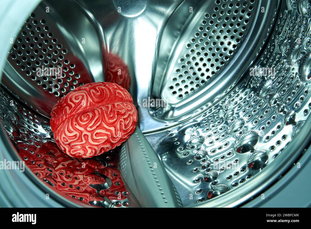 Menschliches Gehirn aus rotem Gummi in einer Waschmaschine, Gehirnwäschekonzept. Stockfoto
