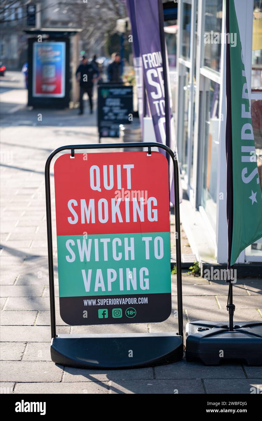 Ein großes Straßenschild, das die Leute auffordert, mit dem Rauchen aufzuhören und zum Dampfen zu wechseln. Das Schild ist auf einem Straßenpflaster außerhalb eines Dampfladens platziert Stockfoto