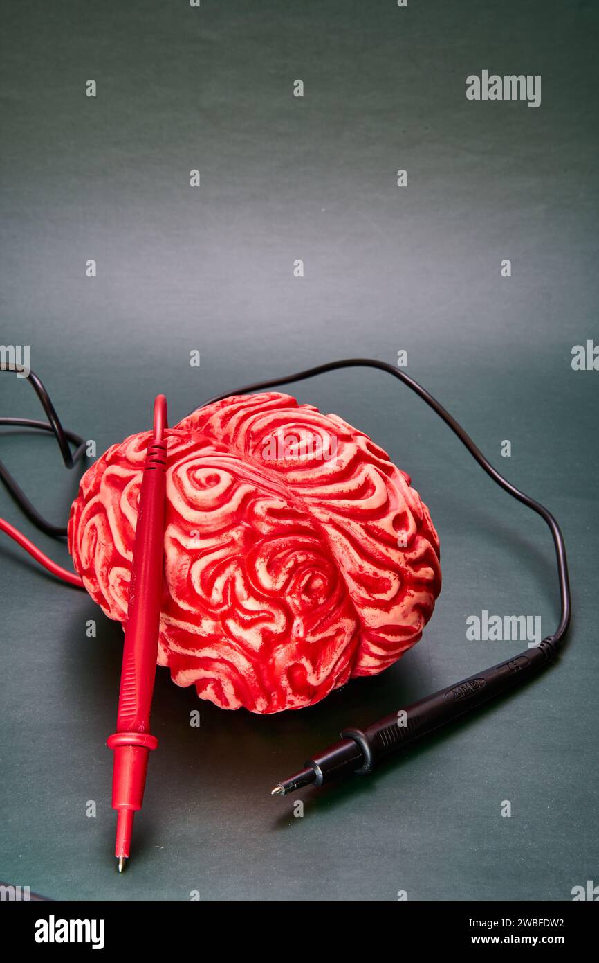 Rotes Gehirn mit roten und schwarzen Elektroden auf grüner Oberfläche. Das Konzept des Kopfschmerzes, der Migräne. Stockfoto