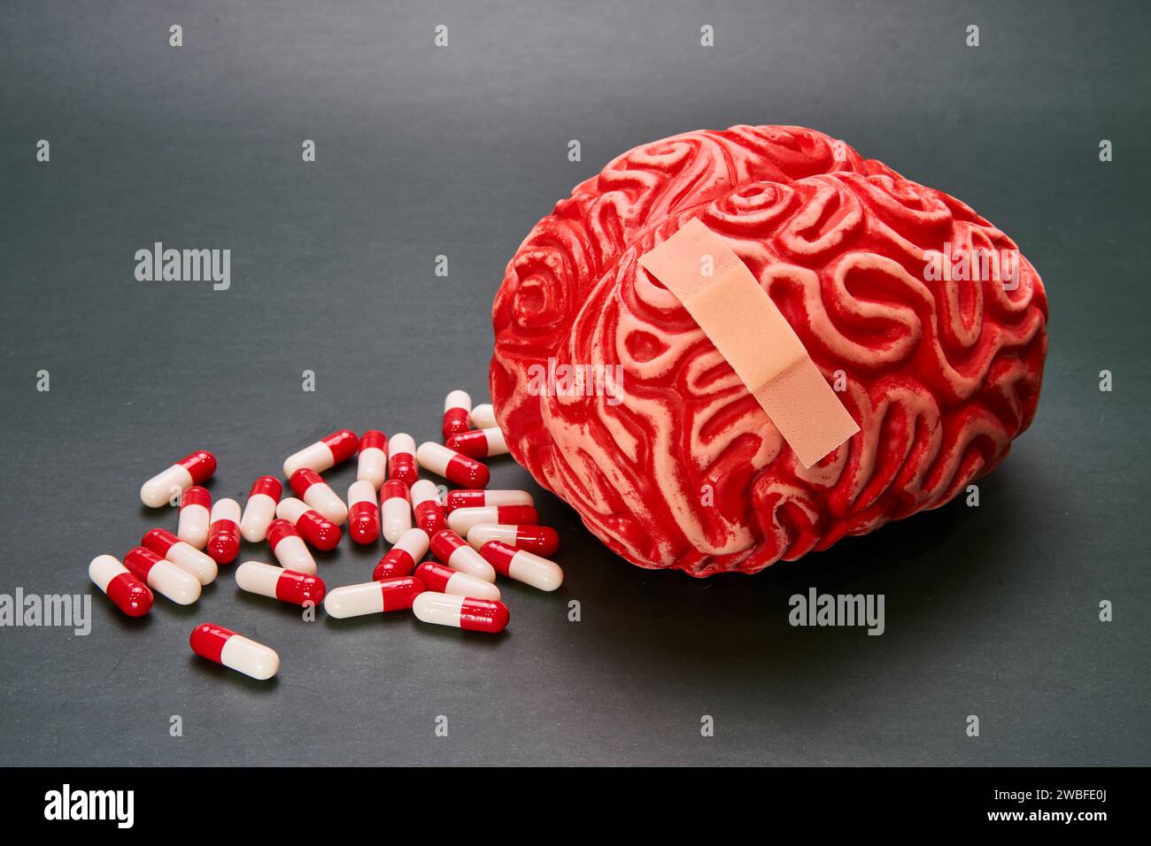 Darstellung eines roten menschlichen Gehirns mit einem Haufen Kapseln, Pillen und einem Pflaster auf dunklem Hintergrund. Stockfoto
