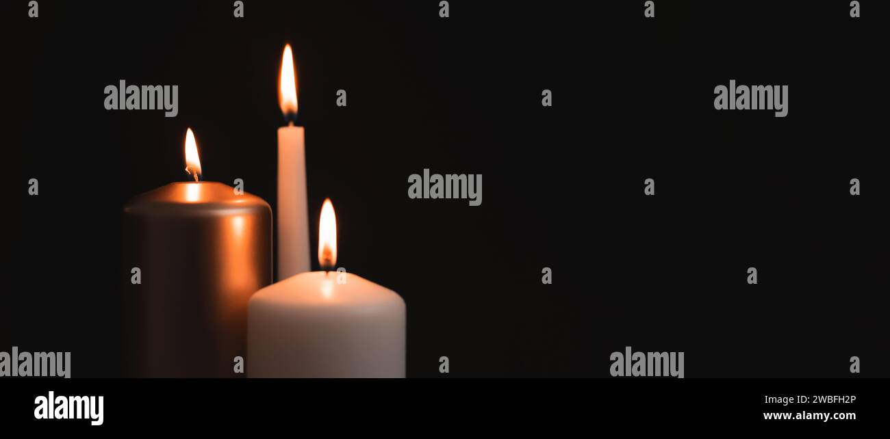 Kerzen brennen in der Dunkelheit über schwarzem Hintergrund. Gedenken, nekrologisches Hinweiskonzept. Stockfoto