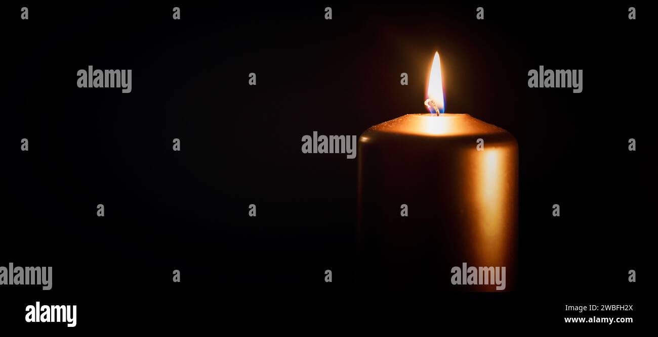 Kerze brennt in der Dunkelheit über schwarzem Hintergrund. Gedenken, nekrologisches Hinweiskonzept. Stockfoto
