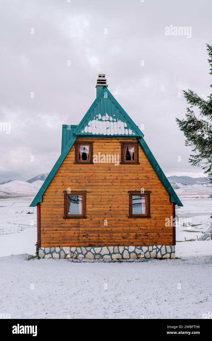 Holzhaus mit grünem Dach in einem schneebedeckten Bergtal Stockfoto