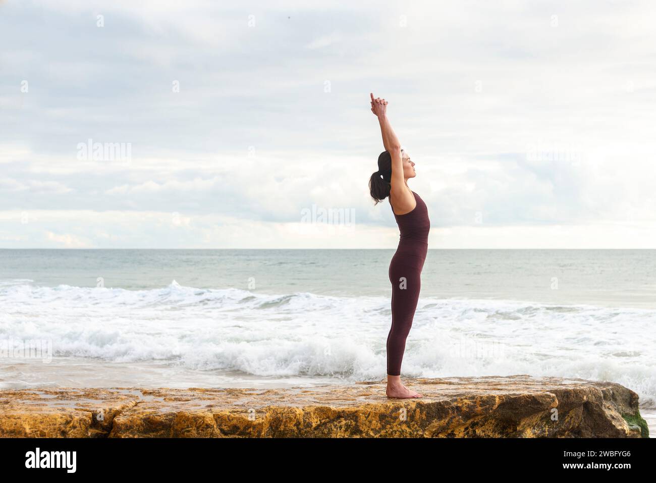 Sportliche Frau, die auf einem Felsen am Meer steht und Yoga übt und sich dehnt Stockfoto