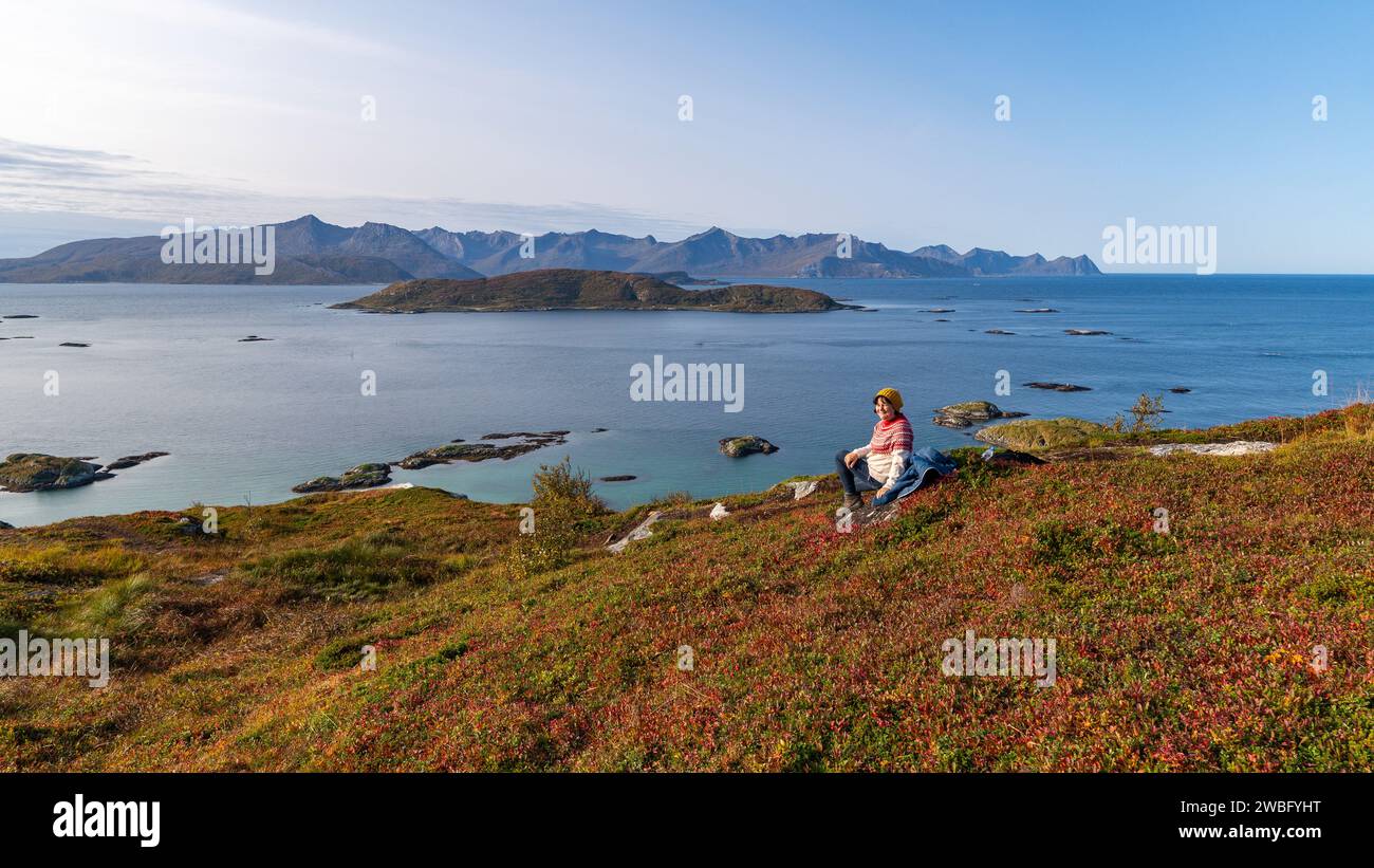 Fröhliche Wanderfrau in der herbstlichen Natur Norwegens. Wandern am Fjord und den Bergen auf der Insel Kvaløya in Troms, orange, grüne, rote Pflanzen Stockfoto