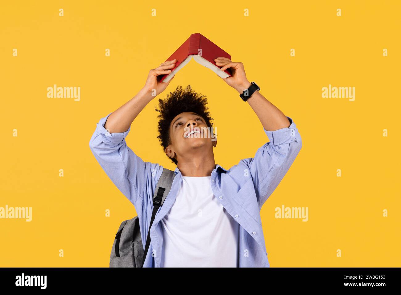 Fröhlicher Schüler mit Bücherdach über Kopf auf gelbem Hintergrund Stockfoto