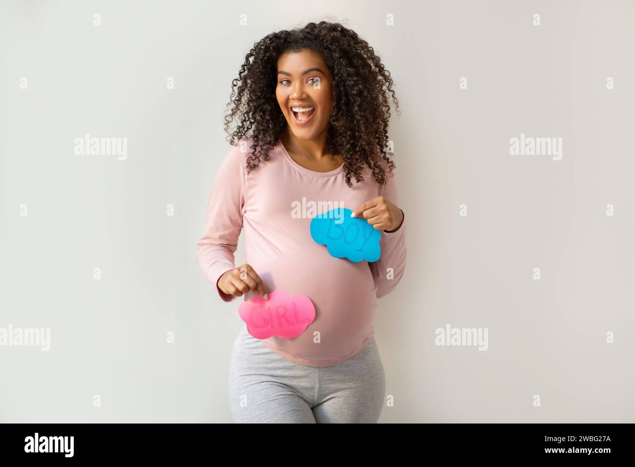 Fröhliche schwarze schwangere Frau, die aufgeregt rosa „GIRL“- und blaue „BOY“-Schilder hält Stockfoto
