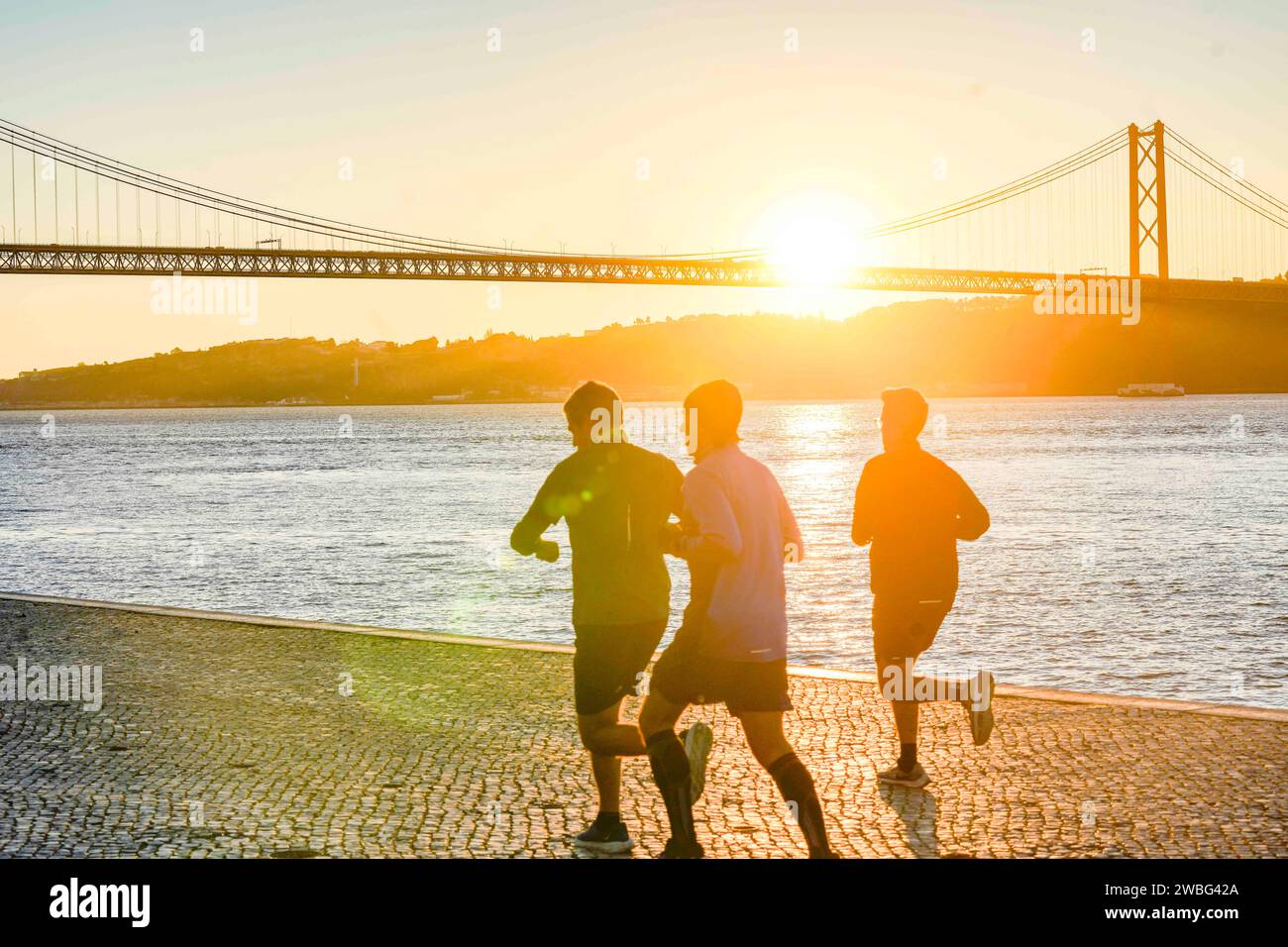 Lissabon, Portugal. Jogger am frühen Morgen am Fluss Tejo. Ein Mann, der die Zeit überprüft. Ponte de 24 Abril im Hintergrund. Stockfoto