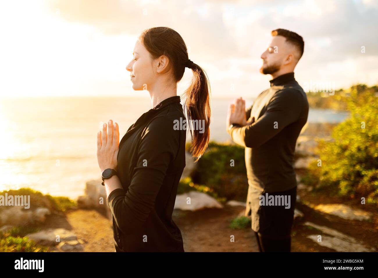 Ein Mann und eine Frau, die bei Sonnenuntergang im Freien meditieren Stockfoto