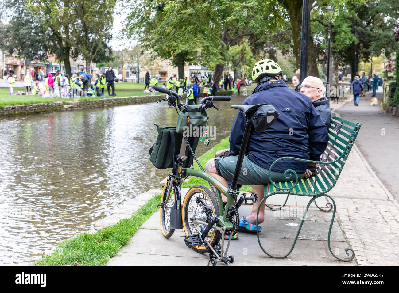 Männlicher Radfahrer in Bourton auf dem Wasser mit einer Brompton x Bear Grylls C Line Erkunden Sie das Faltrad, unterhalten Sie sich mit einem Freund aus England, Großbritannien, 2023 Stockfoto