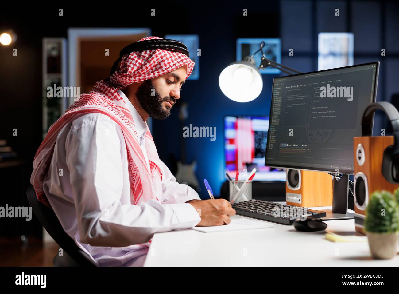 Muslimischer Mann sitzt an einem Computer und Programmen und stellt den Entwicklungsprozess der App vor. Seitenansicht eines Computermonitors mit Algorithmen, die von einem traditionell gekleideten arabischen Mann erstellt wurden. Stockfoto