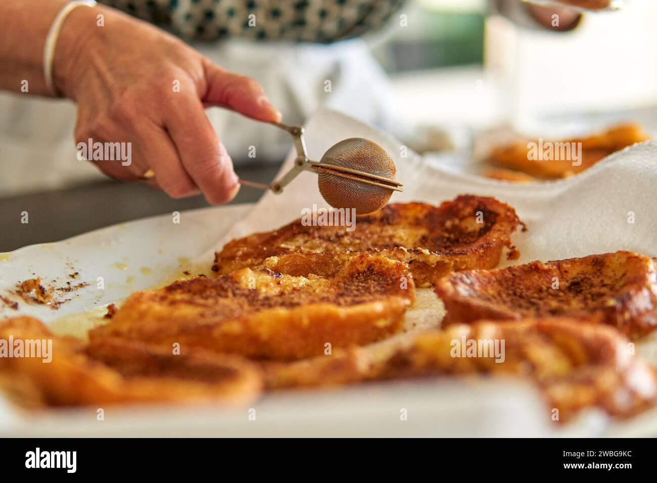 Nahaufnahme der Hand einer nicht erkennbaren älteren Frau, die Zimt auf traditionelle Ostertorrijas streut Stockfoto