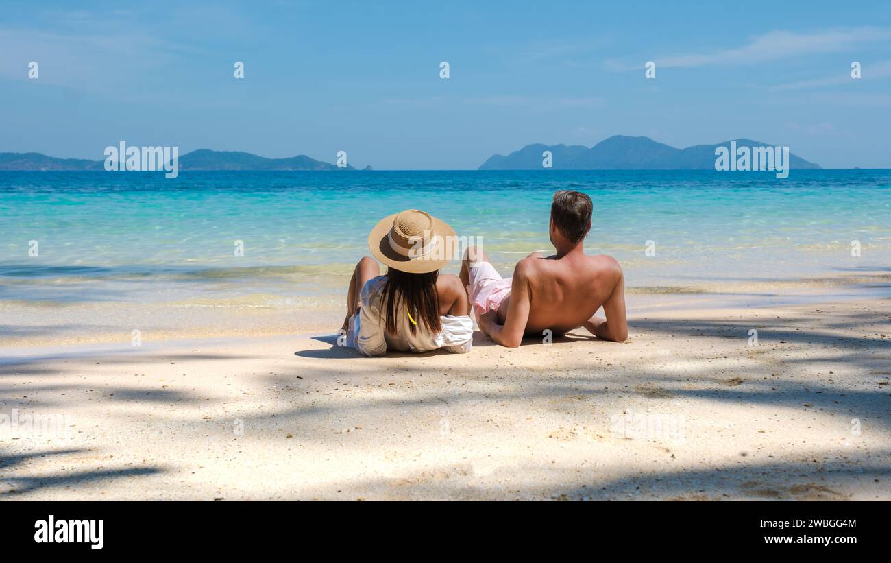 Ein junges Paar Männer und Frauen, die während eines Luxusurlaubs in Thailand an einem tropischen Strand sitzen, diverse Paare, die sich am Strand von Koh Wai I niederlegen Stockfoto